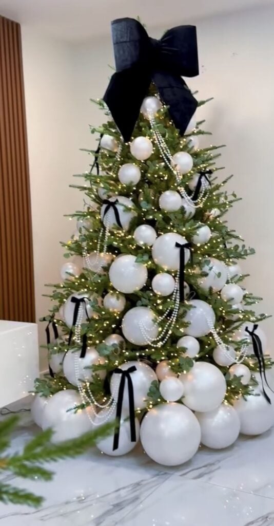 Christmas tree decorated with black bows, white ornaments, and pearl accents for an elegant black and white holiday look.
