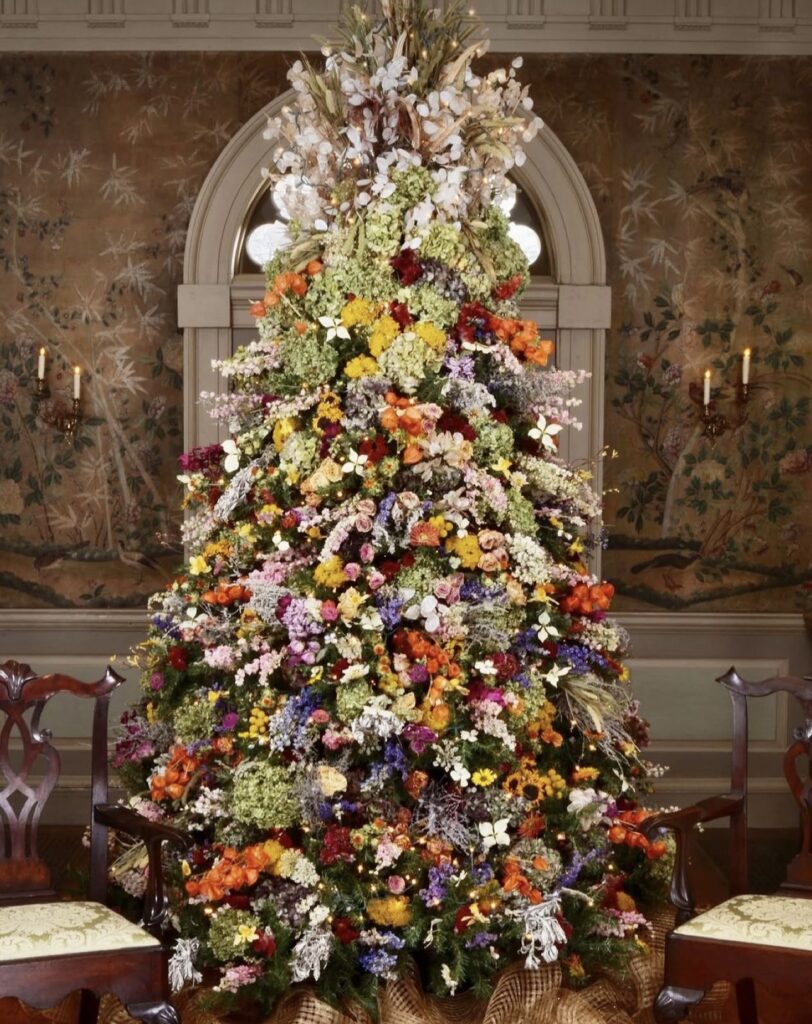 Elegant Christmas tree covered with flowers, greenery, botanical stems, ornaments, and glowing lights for a garden-inspired holiday display.