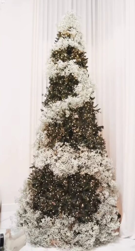 Christmas tree styled with large flowers, greenery, ornaments, ribbon, and floral picks for a lush botanical look.