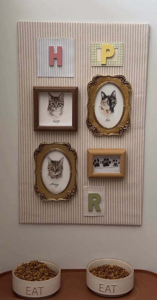 Cat feeding station with striped gallery wall featuring framed cat portraits, paw prints, colorful initials, and two bowls labeled Eat.