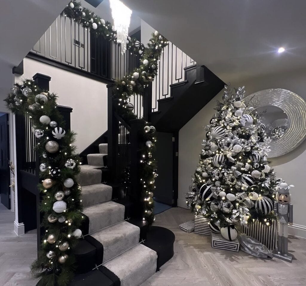 Elegant black and white Christmas tree displayed beside a staircase with oversized ornaments, ribbon, and polished holiday decor.