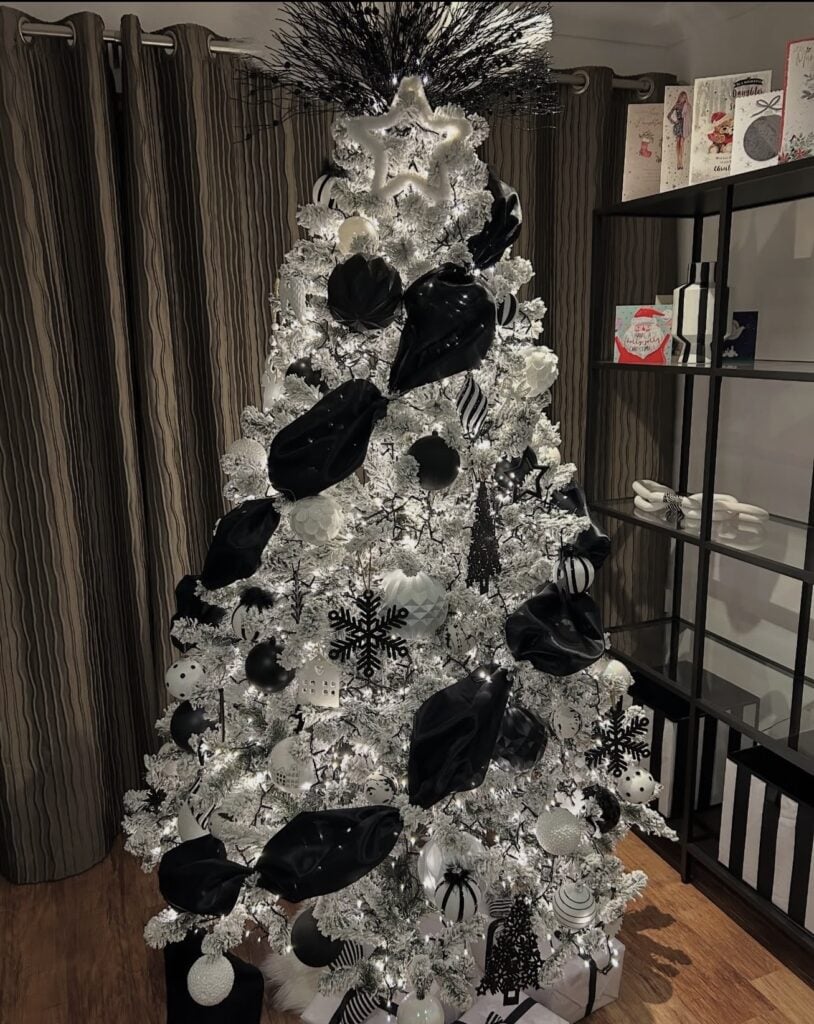 Flocked Christmas tree wrapped with bands of black ribbon and decorated with black and white ornaments.