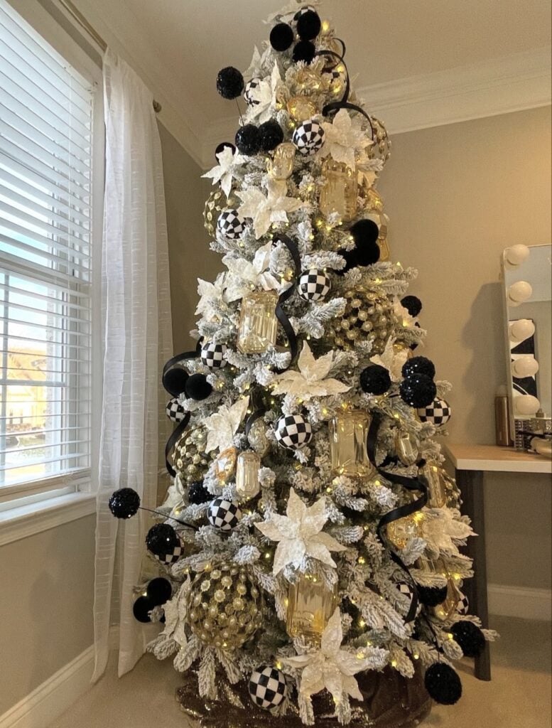 Flocked Christmas tree decorated with black, white, and gold ornaments and layered metallic Christmas accents.