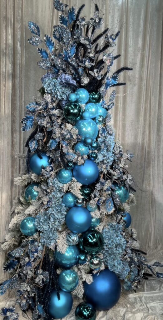 Blue floral Christmas tree decorated with blue flowers, coordinating ornaments, greenery, and elegant holiday accents.