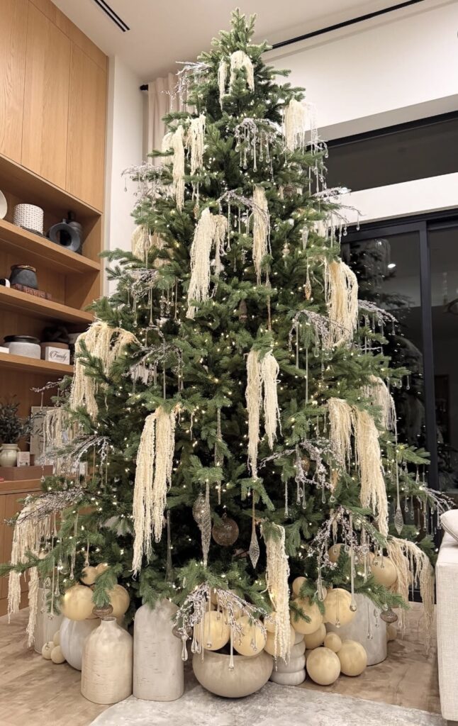 Floral Christmas tree decorated with layered flowers, greenery, ornaments, and warm lights for a lush holiday look.
