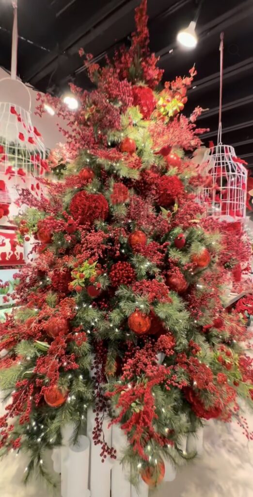 Red floral Christmas tree decorated with red flowers, greenery, ornaments, berries, and festive holiday accents.