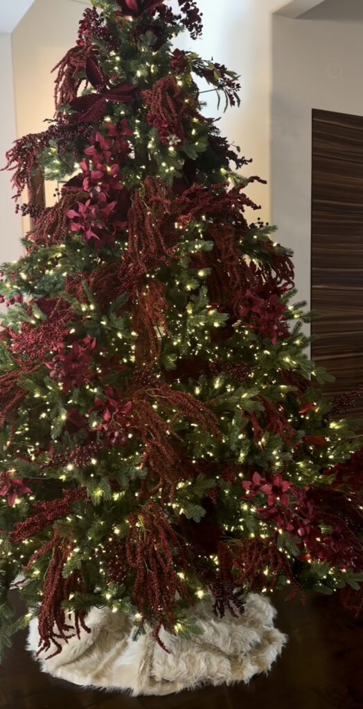 Classic Christmas tree decorated with flowers, traditional ornaments, greenery, ribbon, and warm white lights.