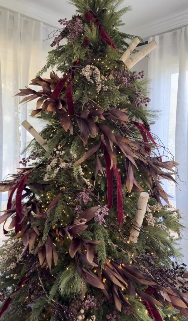 Floral Christmas tree decorated with dried-look burgundy foliage, frosted berries, natural branches, birch accents, velvet ribbon, pinecones, and warm white lights.
