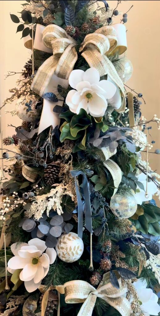 Christmas tree styled with oversized flowers, decorative greenery, ribbon, ornaments, and floral picks for a lush holiday look.