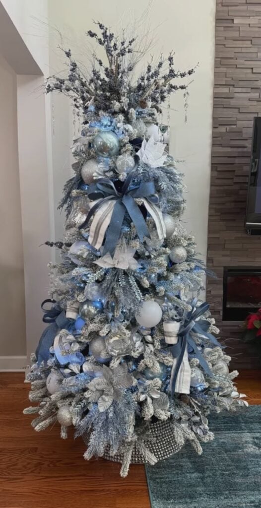 Light blue and silver Christmas tree decorated with icy ornaments, metallic ribbon, sparkling accents, and white lights.