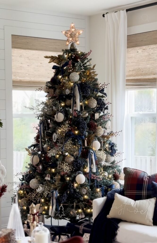 Christmas tree styled with deep navy ornaments, dark blue ribbon, metallic accents, and warm white lights.