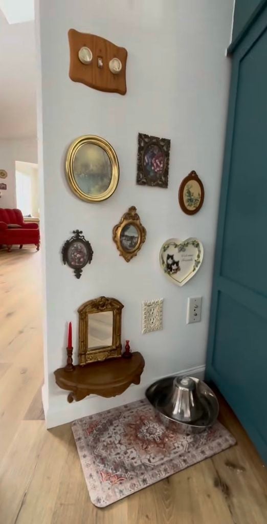 Pet feeding area with an eclectic vintage gallery wall of ornate frames, mirrors, cat art, tiny shelf, candlesticks, and stainless steel bowl.