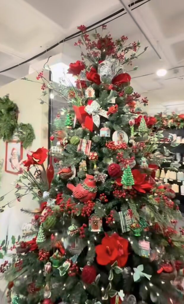 Christmas tree decorated with flowers tucked throughout the branches alongside greenery, ornaments, and botanical stems.