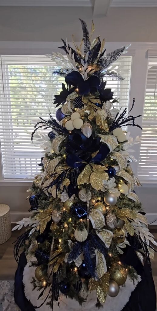 Royal blue and gold Christmas tree decorated with rich blue ornaments, gold ribbon, metallic picks, and warm white lights.