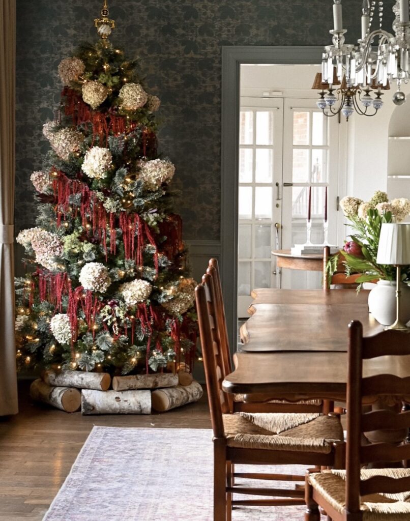 Christmas tree decorated with oversized hydrangeas, greenery, ornaments, and warm holiday lights for a layered floral look.