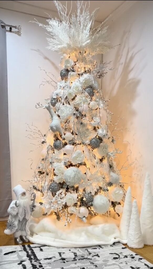 White Christmas tree glowing with warm white lights and decorated with white ornaments, snowy branches, ribbon, and soft luminous accents.