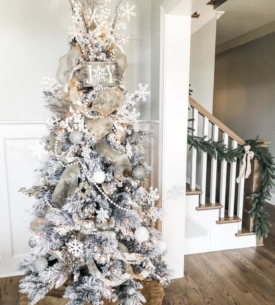 Farmhouse Christmas tree decorated with white ornaments, rustic textures, soft ribbon, snowy accents, warm lights, and neutral holiday decorations.