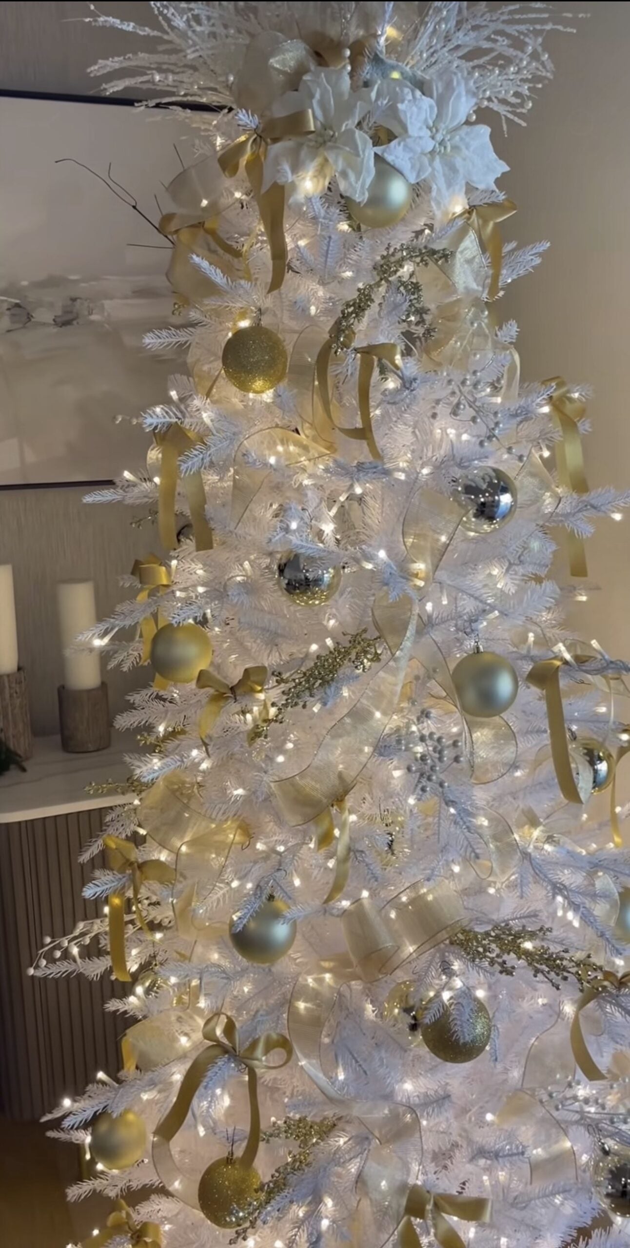 Dramatic all-white Christmas tree layered with white ornaments, ribbon, snowy branches, sparkling accents, and soft warm lights.