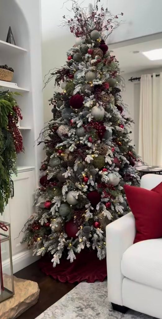 Rich burgundy Christmas tree layered with deep red ribbon, ornaments, berries and greenery for a dramatic holiday look.