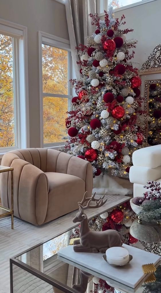 Tall burgundy Christmas tree in a living room covered with velvet bows, deep red ornaments, berries and warm lights.