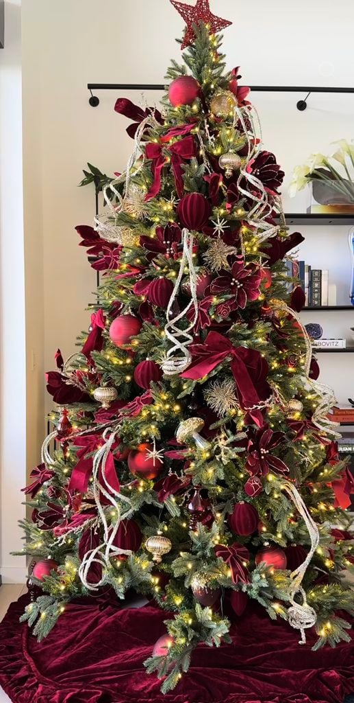 Full burgundy Christmas tree styled with layered wine ornaments, red floral accents, greenery and glowing holiday lights.