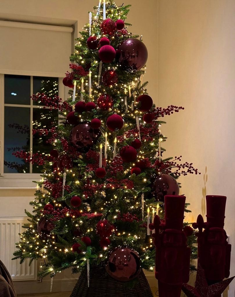Moody burgundy Christmas tree styled with oversized wine-colored ornaments, burgundy berries, candle lights and greenery.
