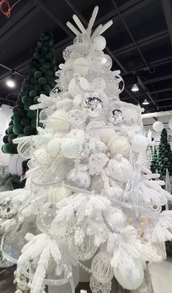 Close view of a heavily decorated white Christmas tree with frosted branches, white and silver ornaments, translucent ribbon, feathers, and sparkling details.