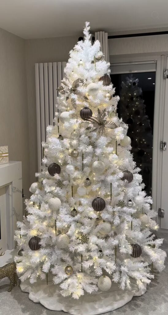 White-decorated Christmas tree styled to coordinate with neutral home decor, featuring pale ornaments, soft ribbon, warm lights, and snowy accents.
