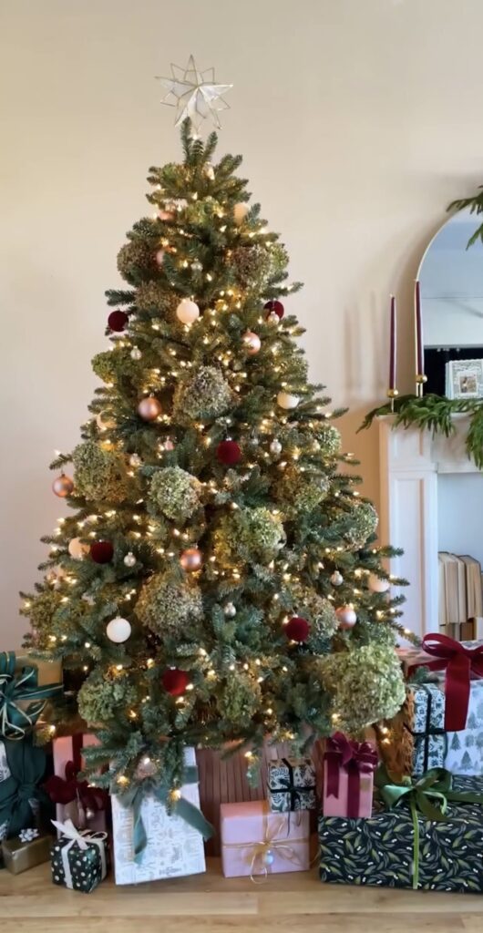 Christmas tree filled with flowers, greenery, ornaments, and decorative stems that add color and texture to the branches.