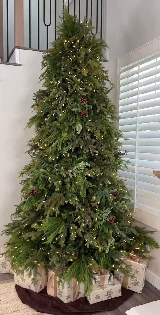 Green-on-green neutral Christmas tree layered with forest green ornaments, greenery, ribbon, and natural textures.