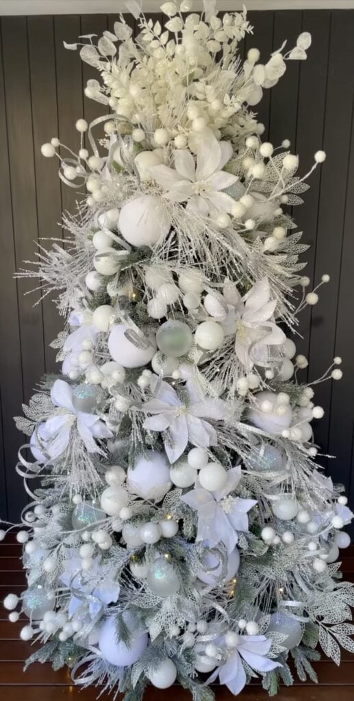 All-white Christmas tree filled with white flowers, round ornaments, frosted berries, silvery leaves, snowy branches, and textured botanical picks.