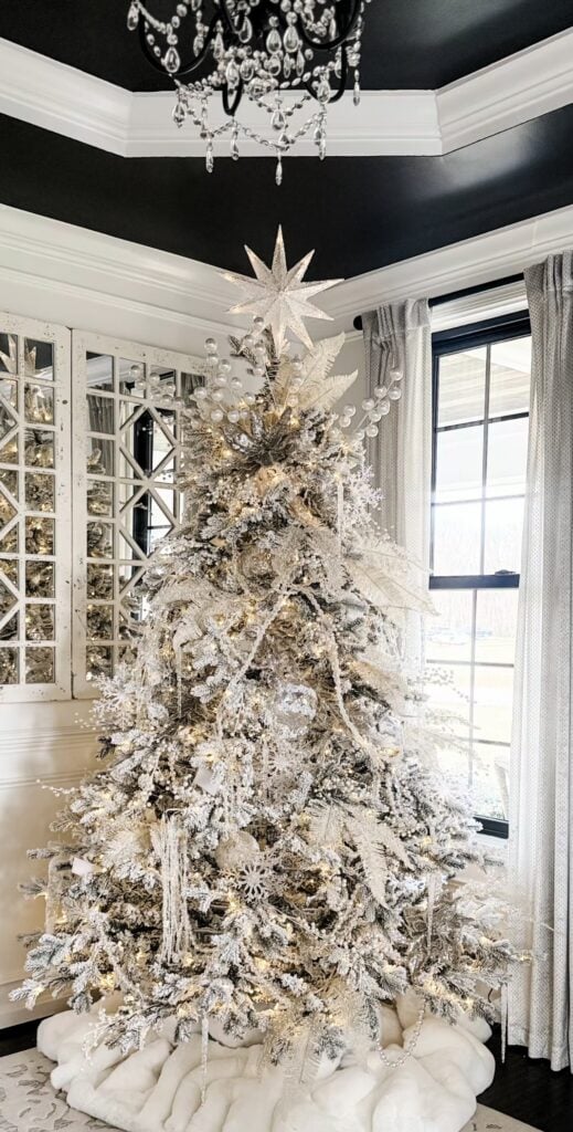 Snow-covered Christmas tree with a glowing star topper, icy branches, white ornaments, hanging icicles, pearl accents, warm lights, and a white tree skirt.