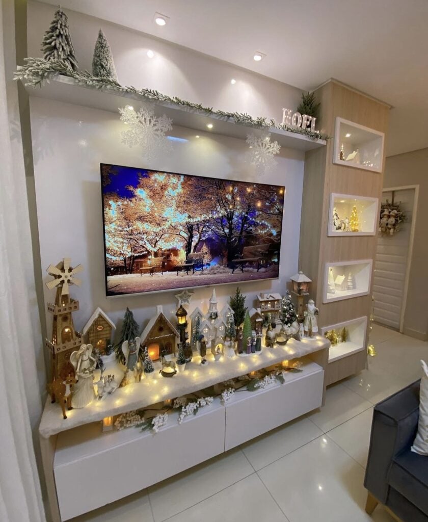 Large Christmas village and nativity display arranged across a white media console with miniature houses, trees, fairy lights, snowflakes, and winter decor.