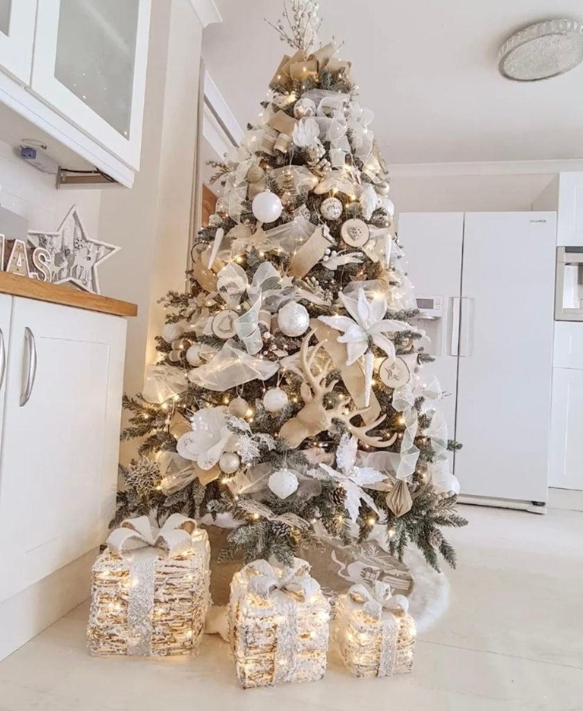 Neutral decorated Christmas tree with soft cream and beige ornaments, ribbon, greenery, and warm holiday lights.