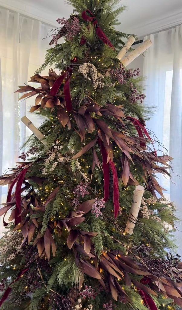 Organic burgundy Christmas tree styled with natural greenery, branches, berry stems, wine velvet ribbon and warm lights.