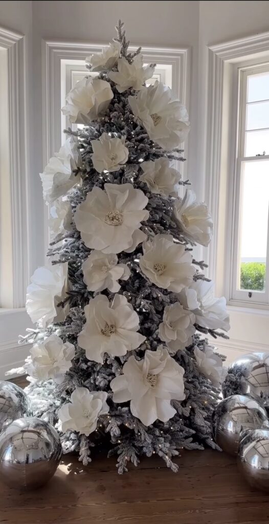 Christmas tree decorated with oversized statement flowers, greenery, ornaments, and botanical accents throughout the branches.