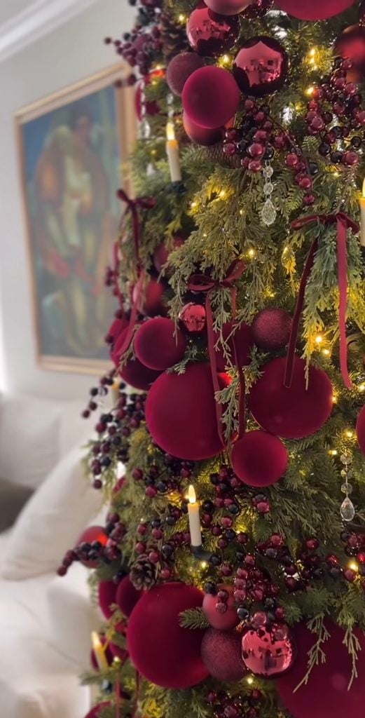 Close-up of a burgundy Christmas tree with velvet ornaments, glossy wine baubles, berries and warm candle-style lights.