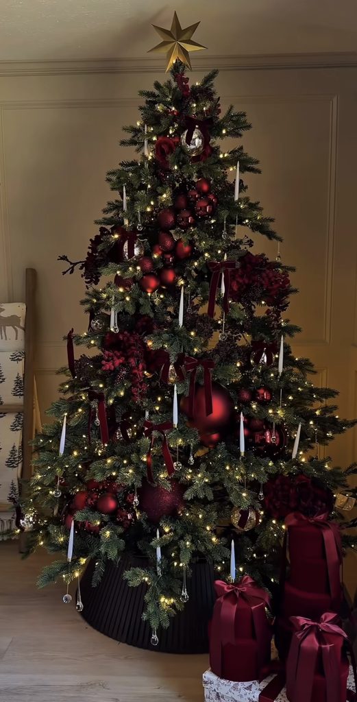 Rich burgundy Christmas tree inspiration with layered red ornaments, decorative ribbon and glowing Christmas lights.