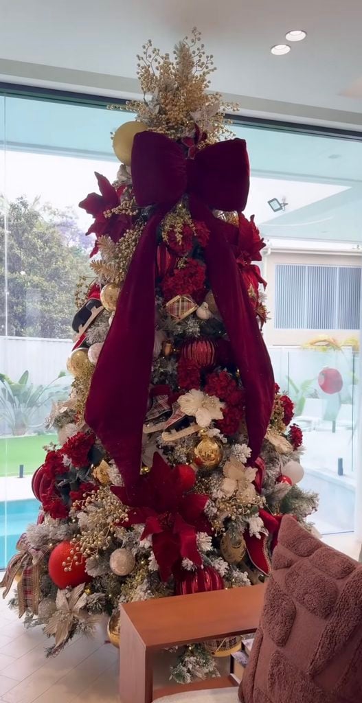 Burgundy Christmas tree with a dramatic oversized bow, deep red ornaments, berries and layered holiday greenery.