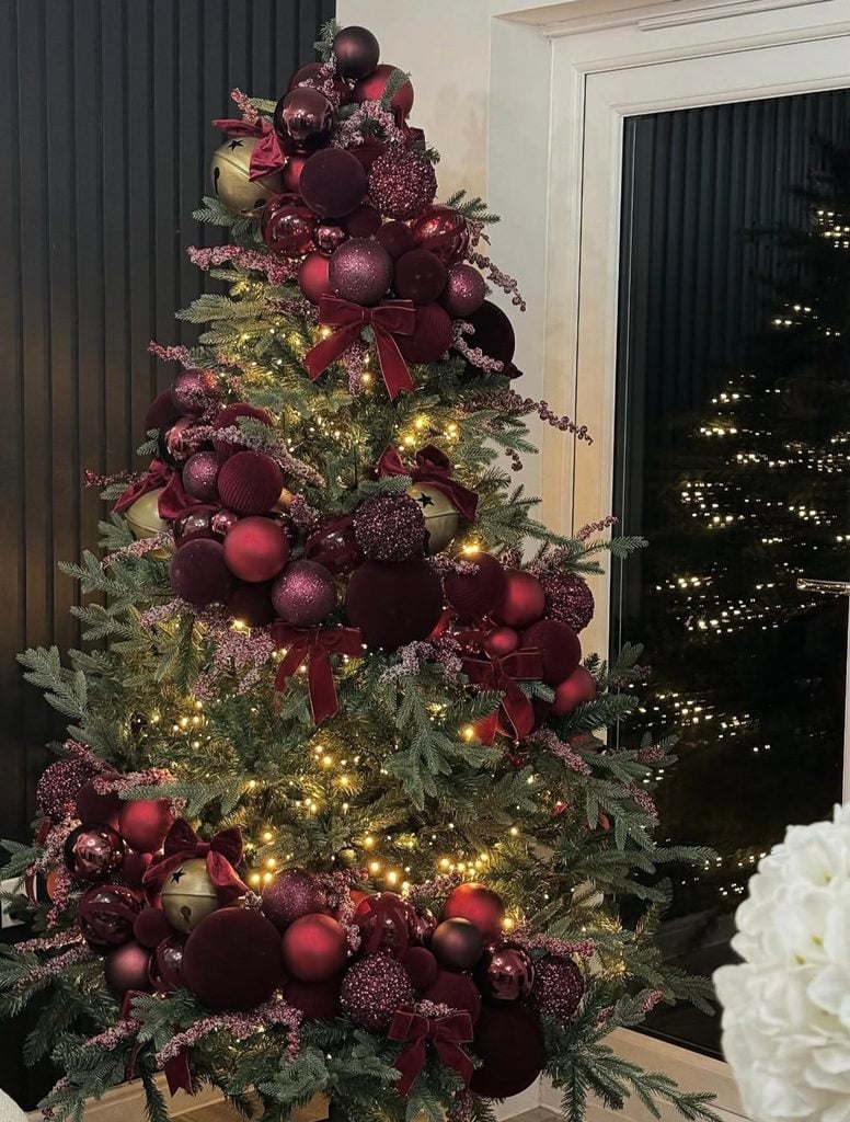 Creative burgundy Christmas tree featuring wrapped and textured ornaments, deep wine accents, greenery and warm lights.