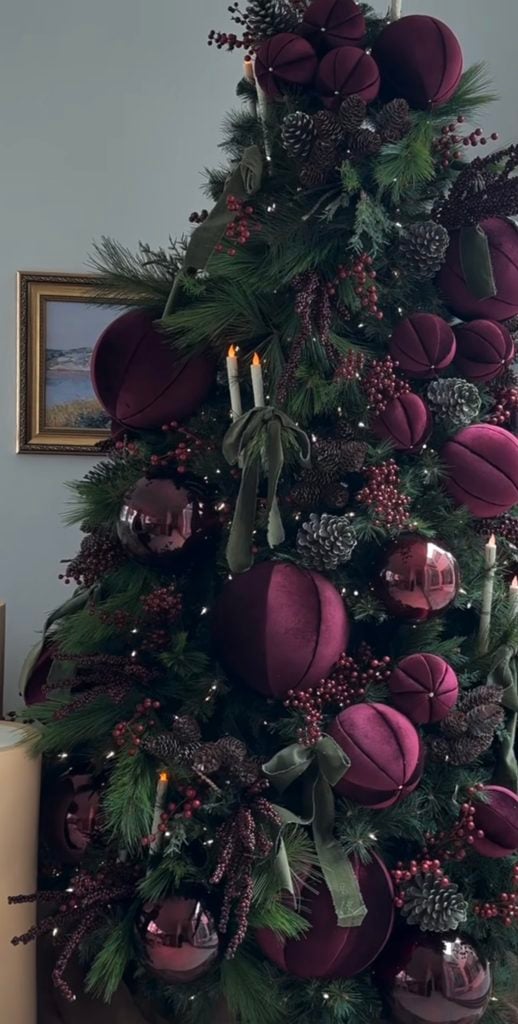 Dark green Christmas tree decorated with rich burgundy velvet ornaments, berry picks, pinecones and warm white lights.