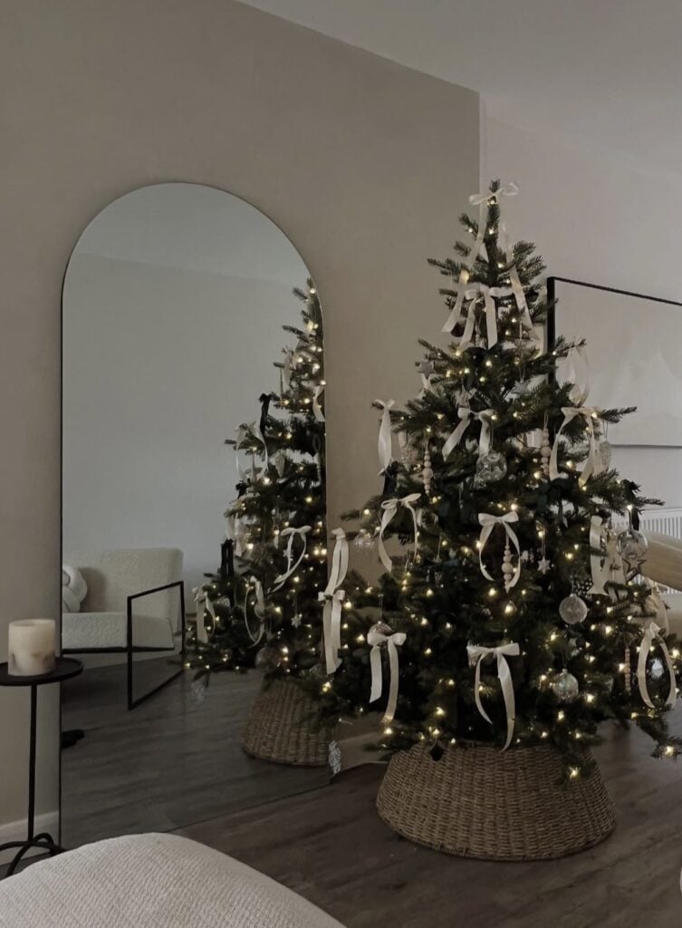 Simply styled Christmas tree decorated with white ornaments, delicate pale accents, understated ribbon, and warm white lights.