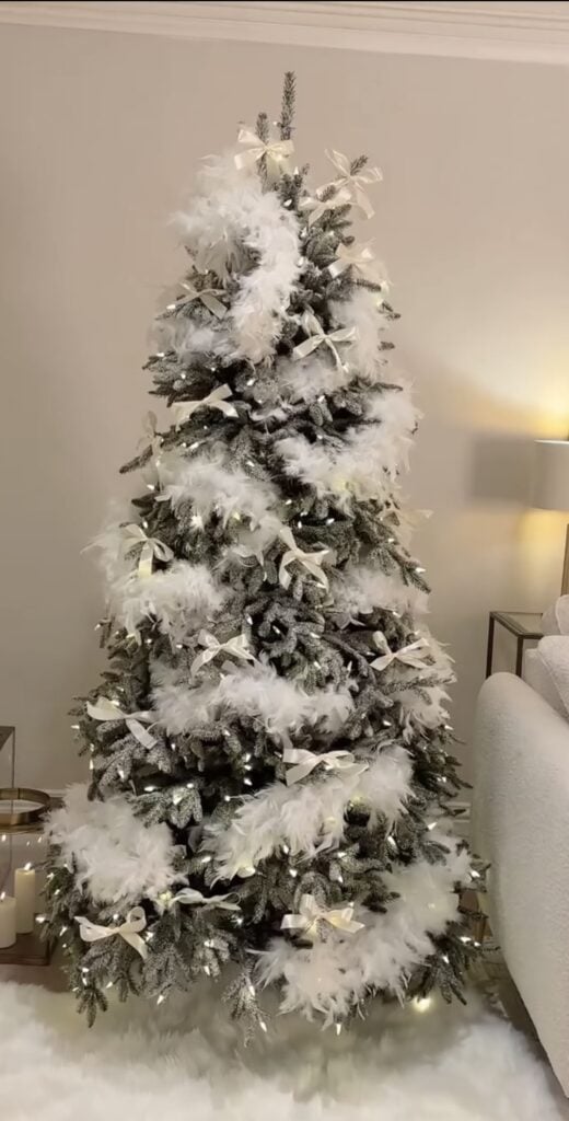 White Christmas tree wrapped in a fluffy feather boa and decorated with pale ornaments, soft textures, and warm holiday lights.