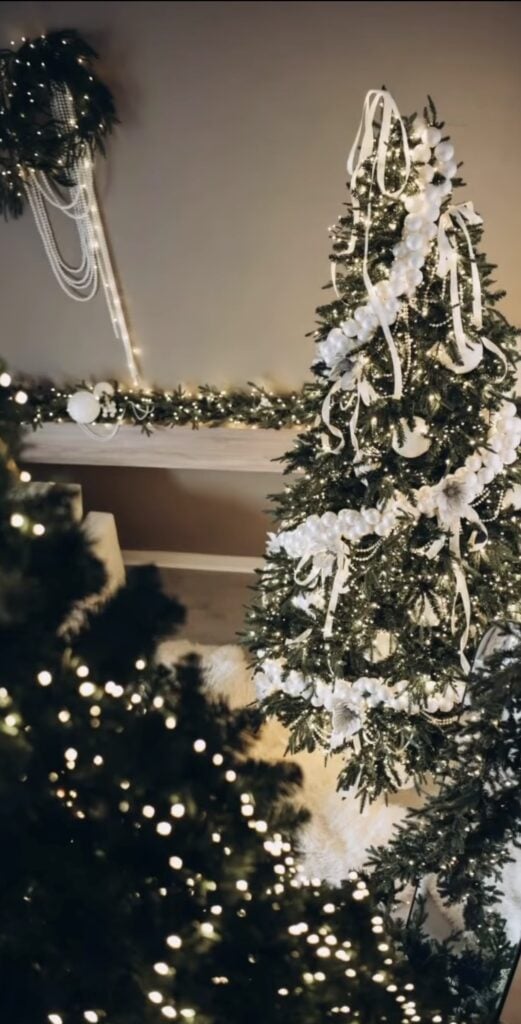 Elaborate white Christmas tree filled with oversized ornaments, layered ribbon, frosted branches, floral picks, sparkling decorations, and warm white lights.