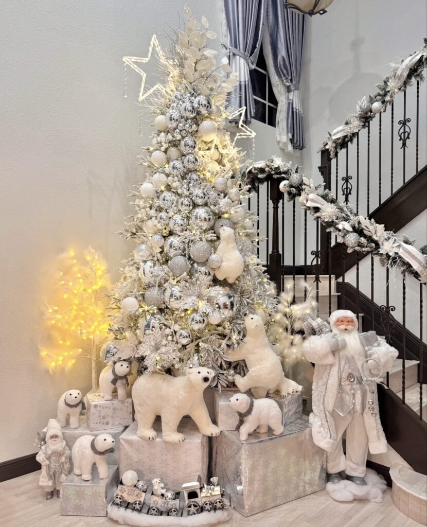 Flocked white and silver Christmas tree decorated with metallic ornaments, glowing star outlines, white polar bears, winter animals, and a white Santa display.