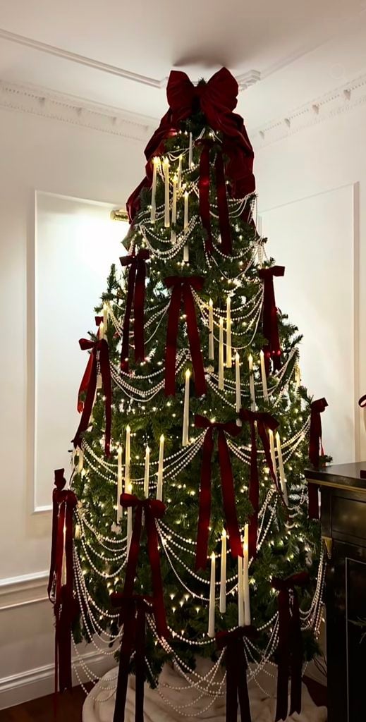 Elegant Christmas tree decorated with burgundy velvet bows, draped pearl garlands, candle-style lights and a large burgundy bow topper.