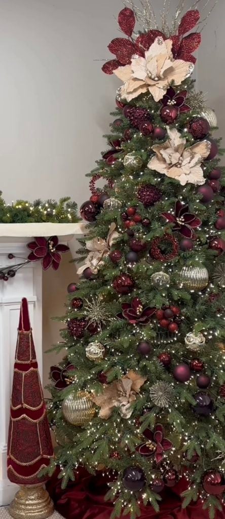 Elegant burgundy Christmas tree decorated with deep red ornaments, cream poinsettias, metallic accents and warm white lights.