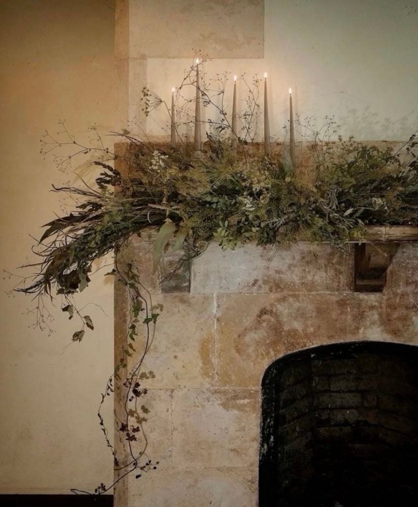 Neutral Christmas fireplace mantel decorated with natural greenery, candles, stockings, and understated seasonal accents.