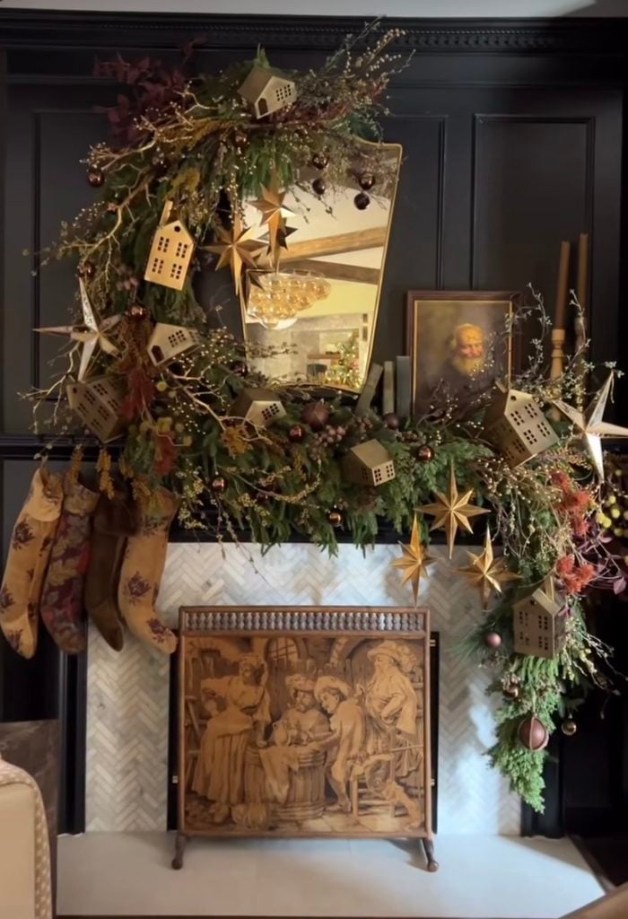 Elaborate Christmas fireplace mantel covered with lush greenery, ornaments, ribbon, and dramatic holiday decorations.
