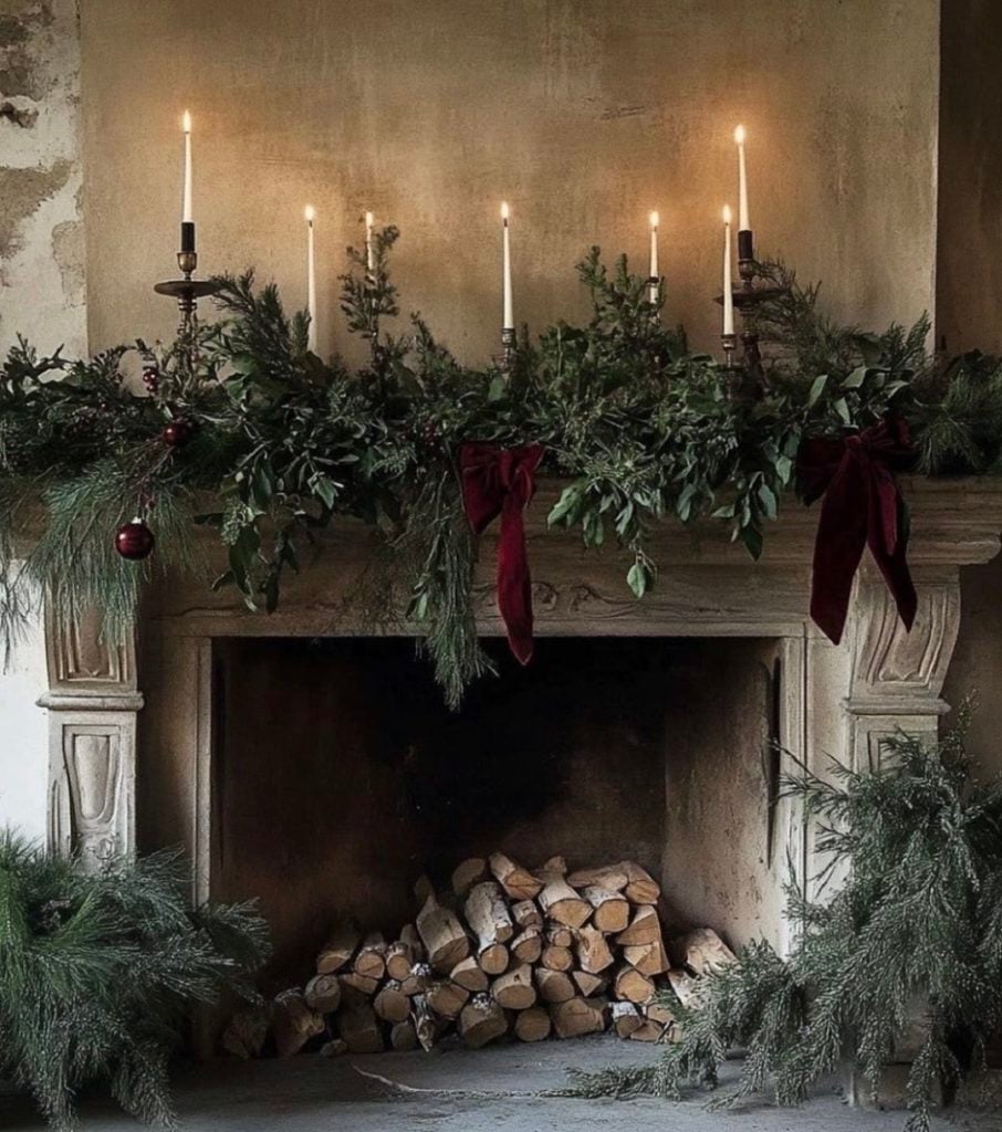 Moody Christmas fireplace mantel styled with dark greenery, glowing candles, and dramatic holiday decor.